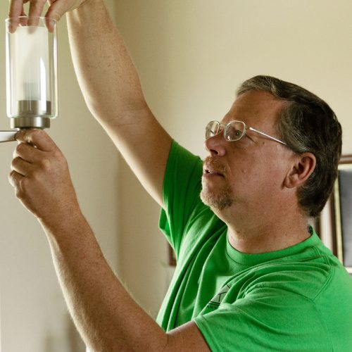 Handyman changing out a lightbulb on a hanging light fixture