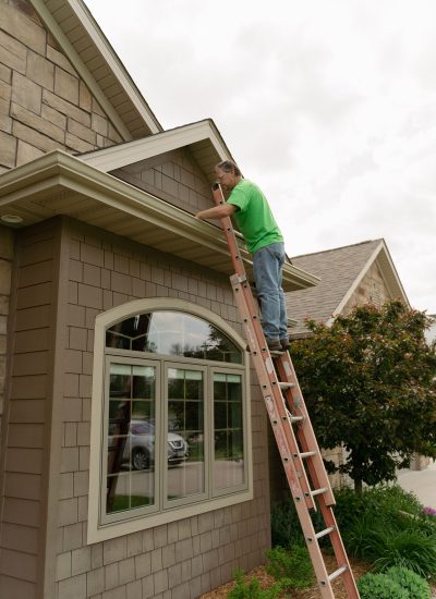 Handyman on a ladder, cleaning leaves out of the gutter