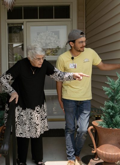 An elderly woman standing on her porch with a handyman, pointing to something outside of the picture