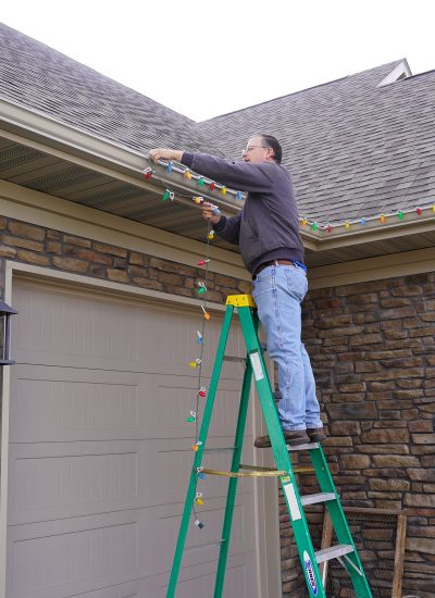 Handyman on a ladder hanging Christmas lights